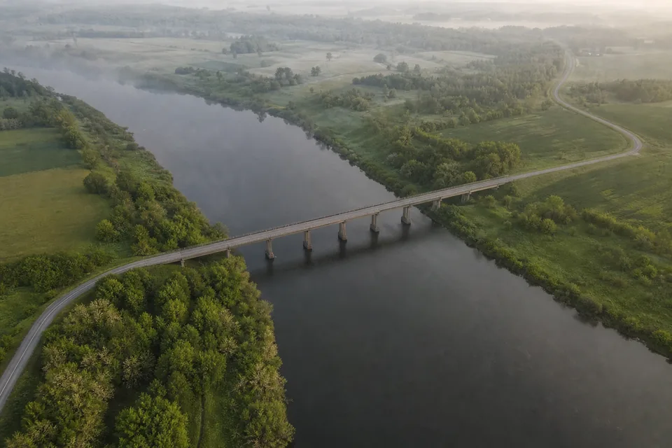 Aerial view of a bridge crossing a wide river between two green rural banks