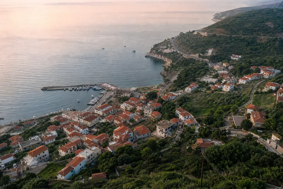 Aerial view of a small coastal town at dawn with a harbor and a road along green hills