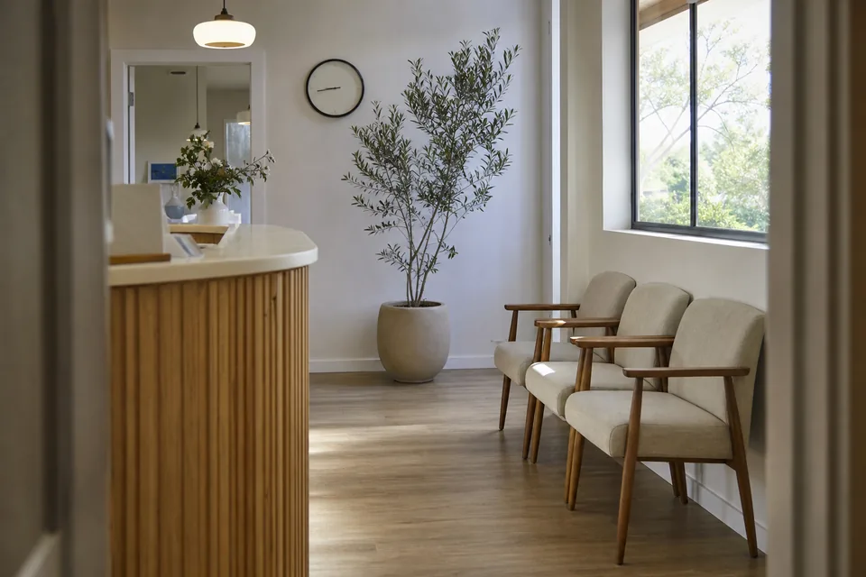 Empty bright reception area of a small clinic with an oak counter, chairs and an olive tree